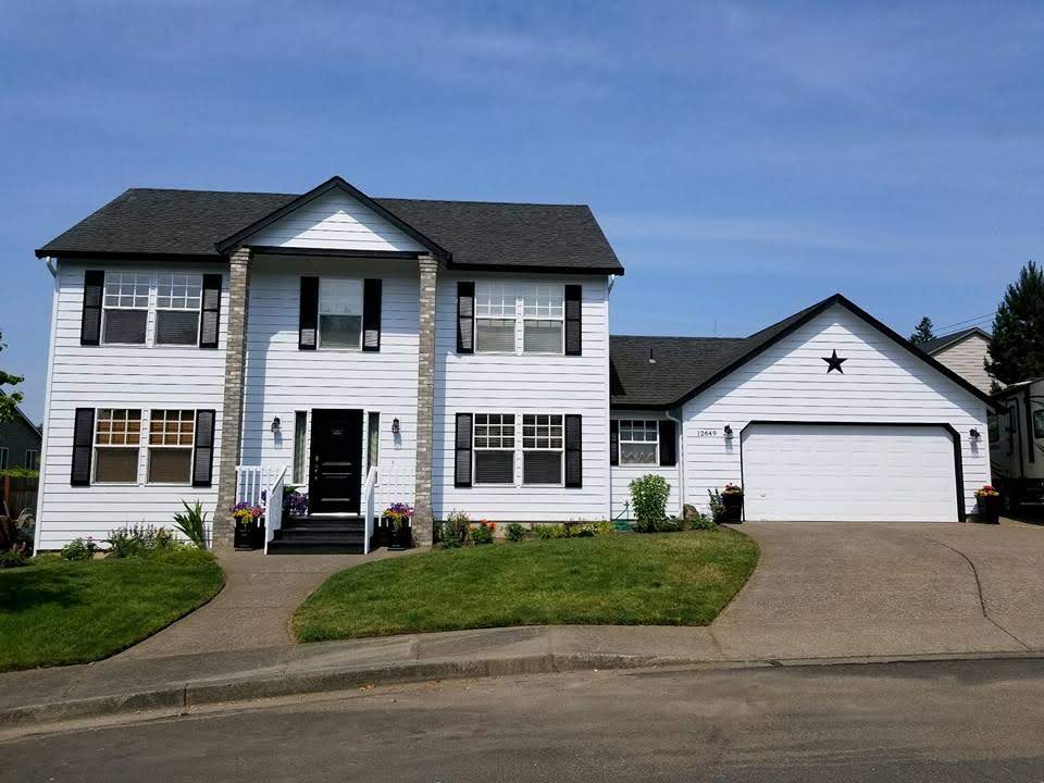 Two-story home with white lap siding and black shutters after an exterior repaint